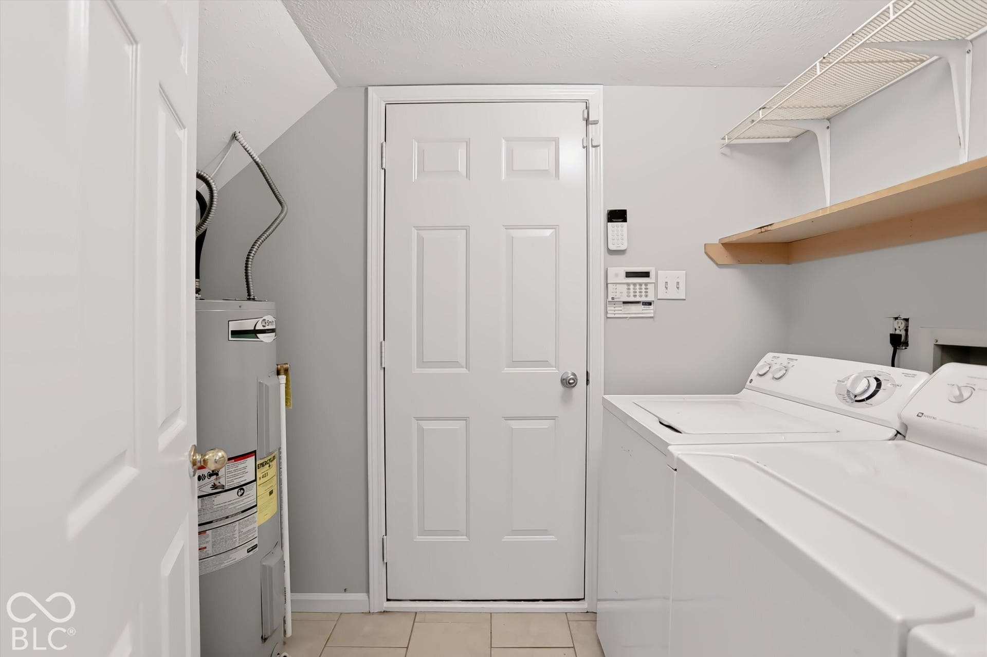 Laundry area featuring a paneled door, tiled flooring, built-in shelving, and a water heater