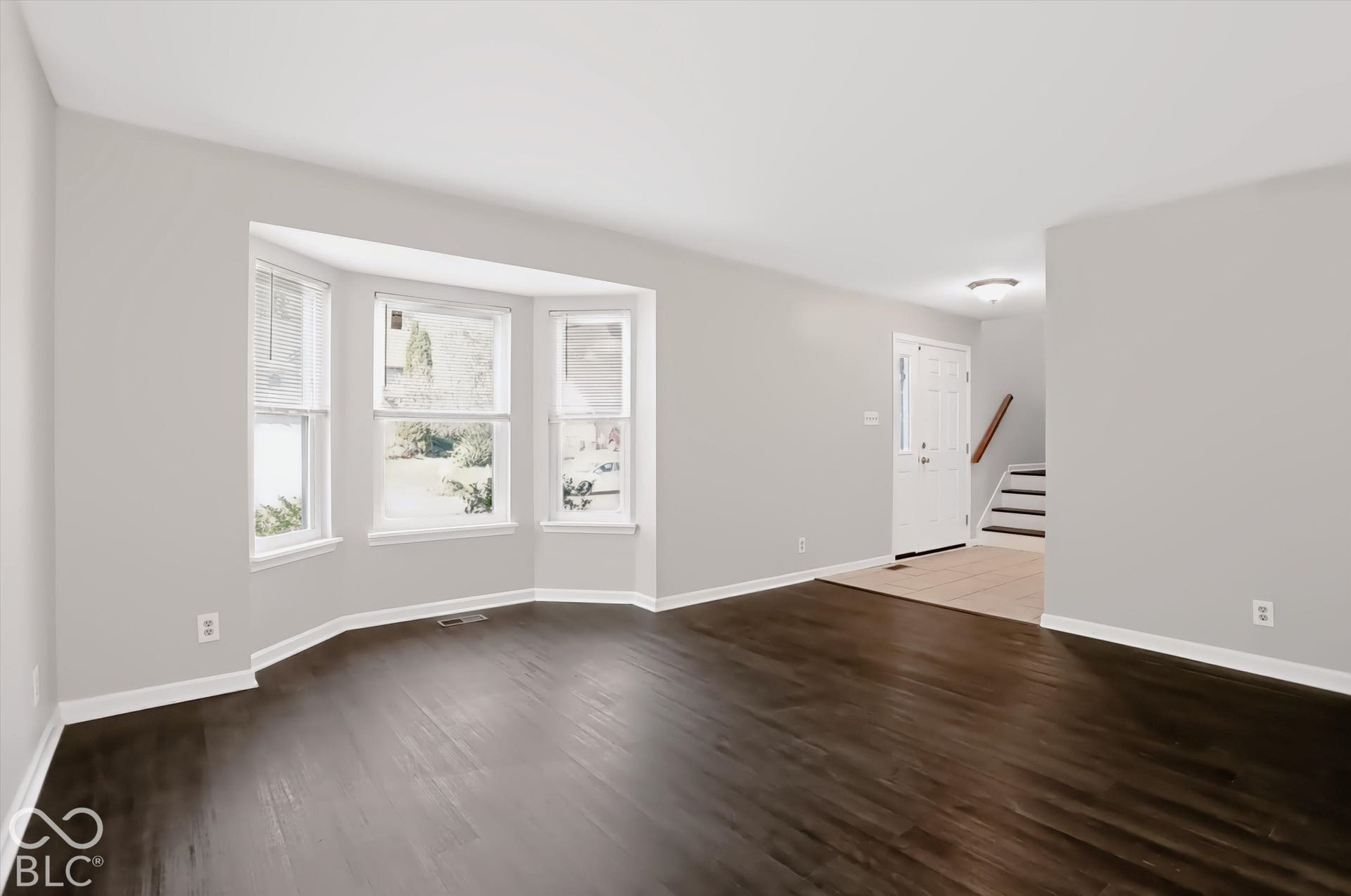 Spacious living area featuring wood-finish flooring, a bay window, and light gray wall tones