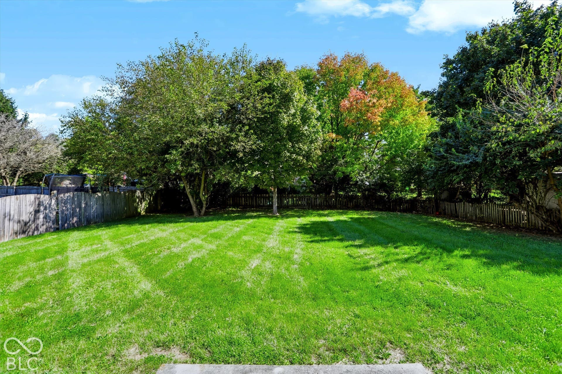 Expansive green lawn with mature trees and a wood fence enclosure