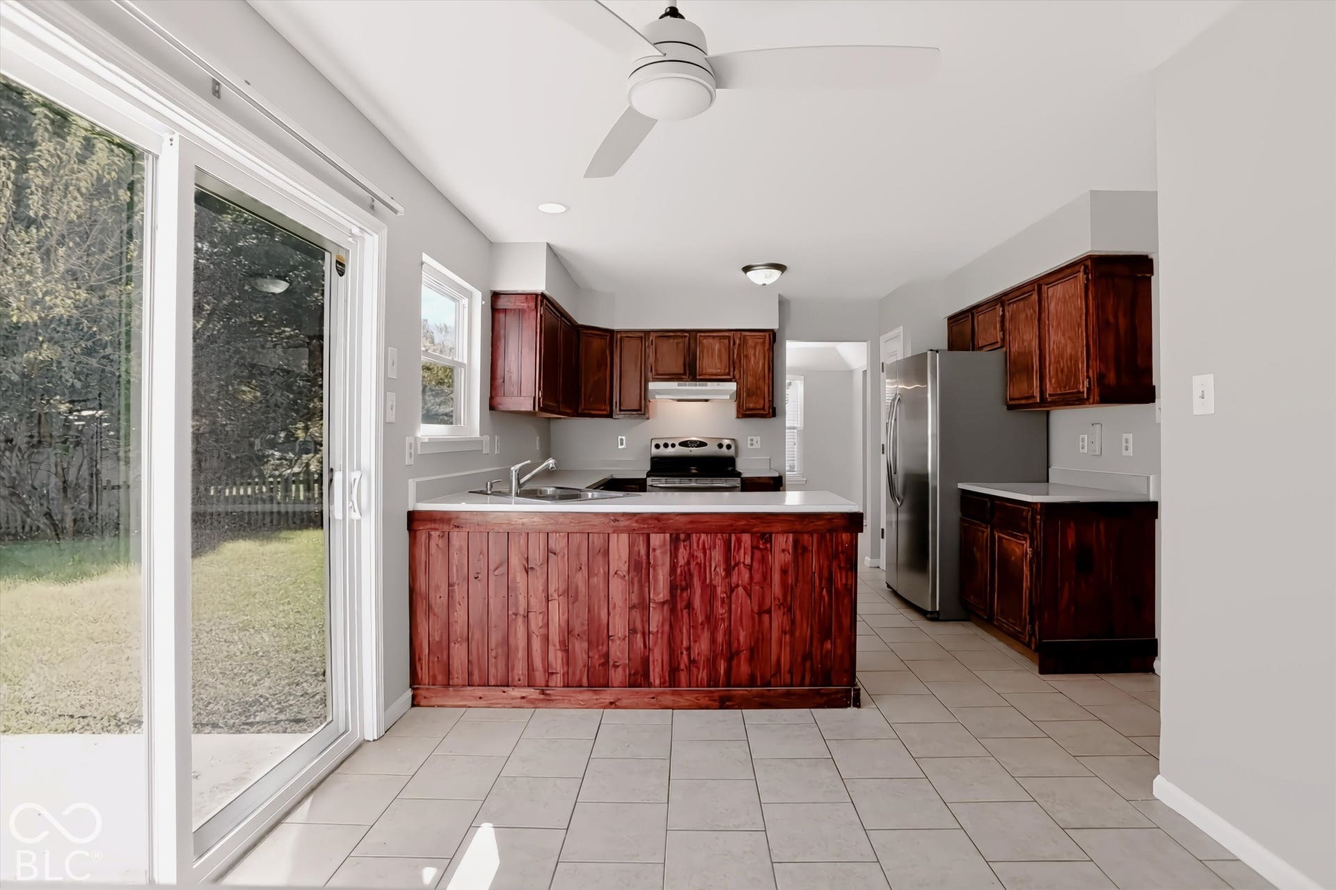 Kitchen featuring wood cabinetry, stainless steel appliances, white countertops, tile flooring, and a ceiling fan