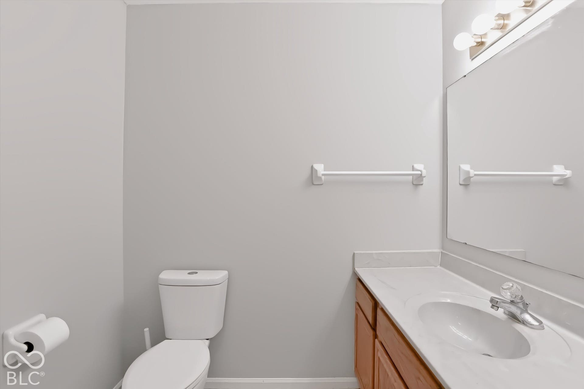 Bathroom featuring a wood-finish vanity with an integrated sink, a large mirror, and wall-mounted lighting