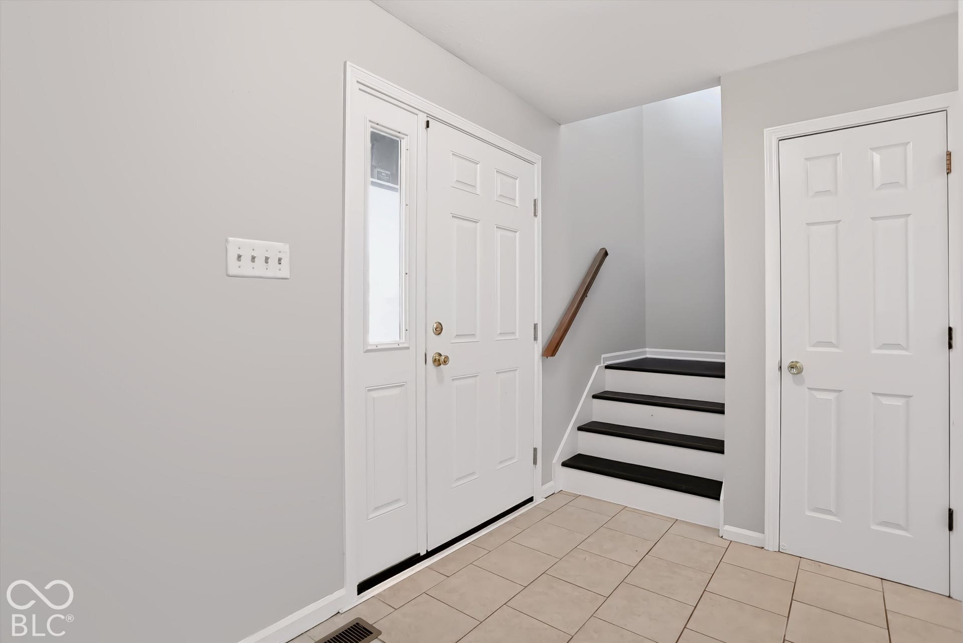Entryway featuring a white paneled door with a sidelight, ceramic tile flooring, and a staircase with a wood handrail