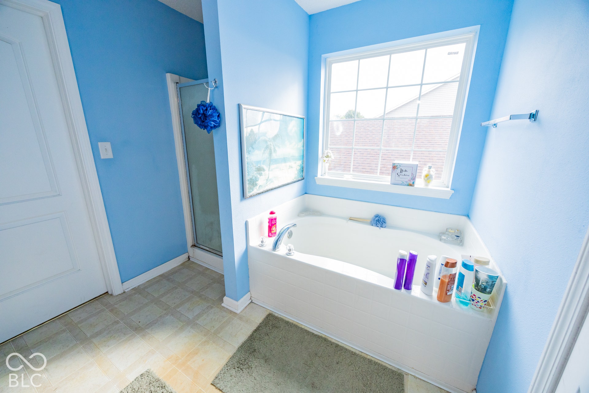 Built-in corner bathtub with a tiled surround, framed window, and a separate shower enclosure