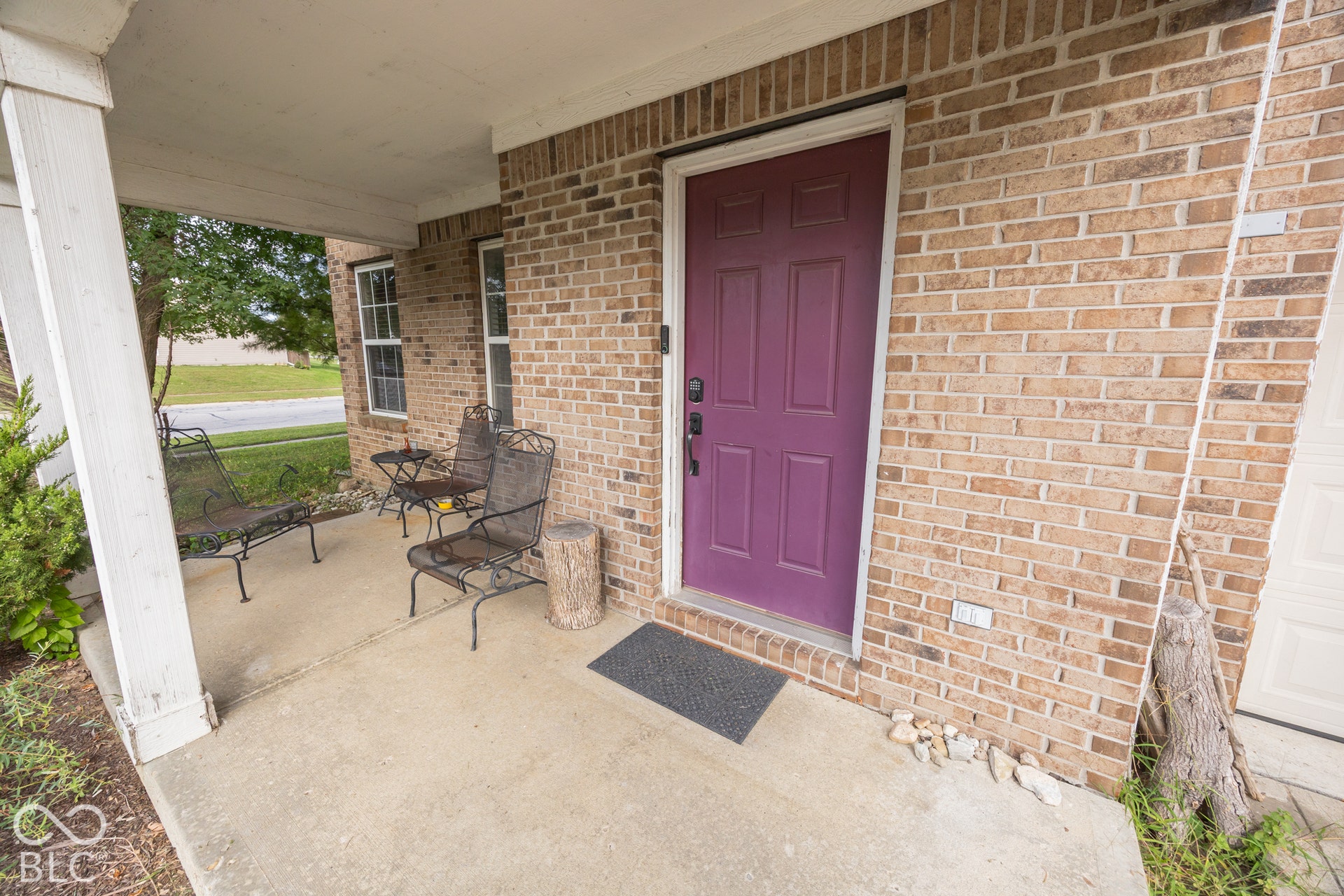 Covered concrete porch with brick facade and vibrant front door