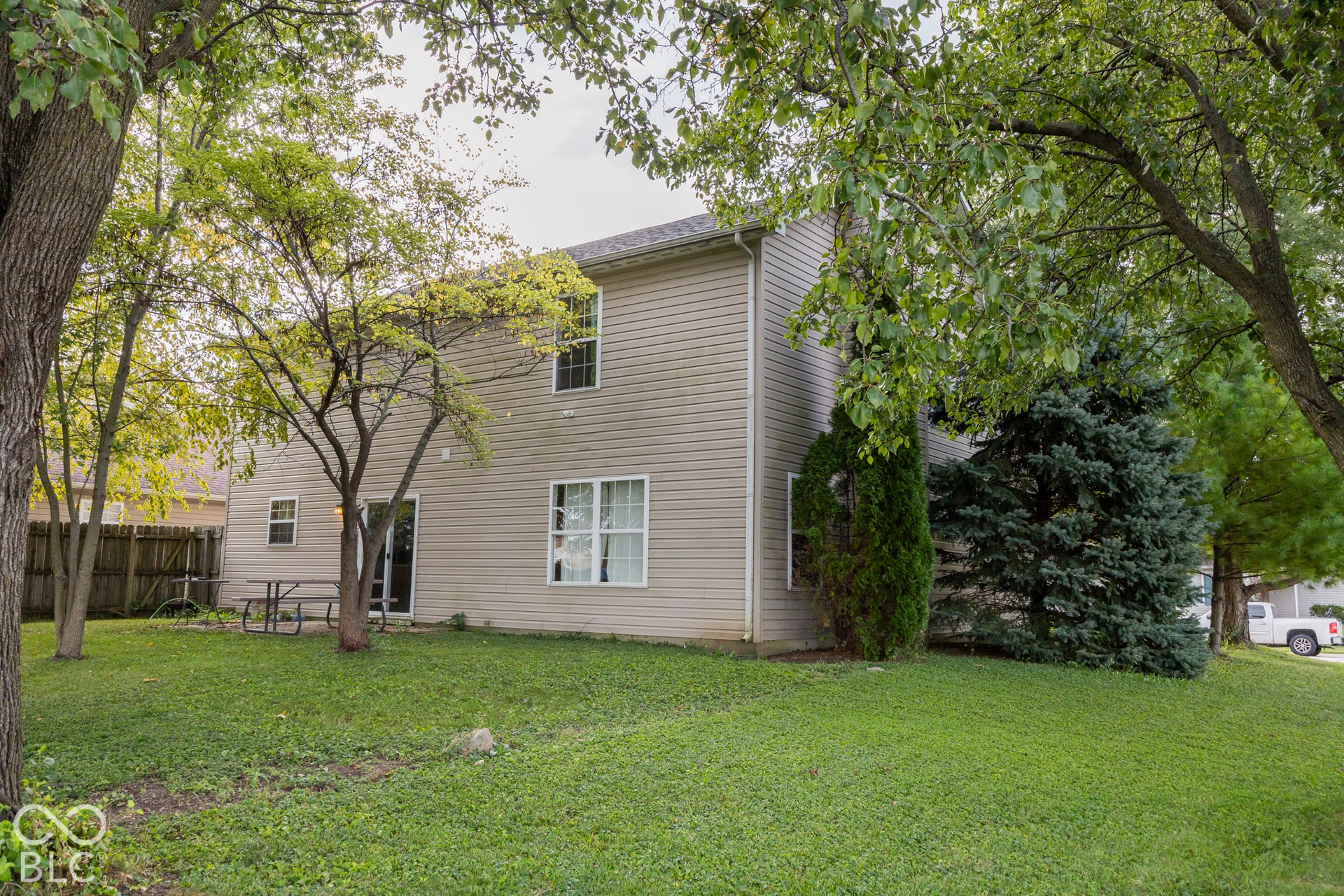Expansive rear yard featuring green ground cover, mature trees, and privacy fencing