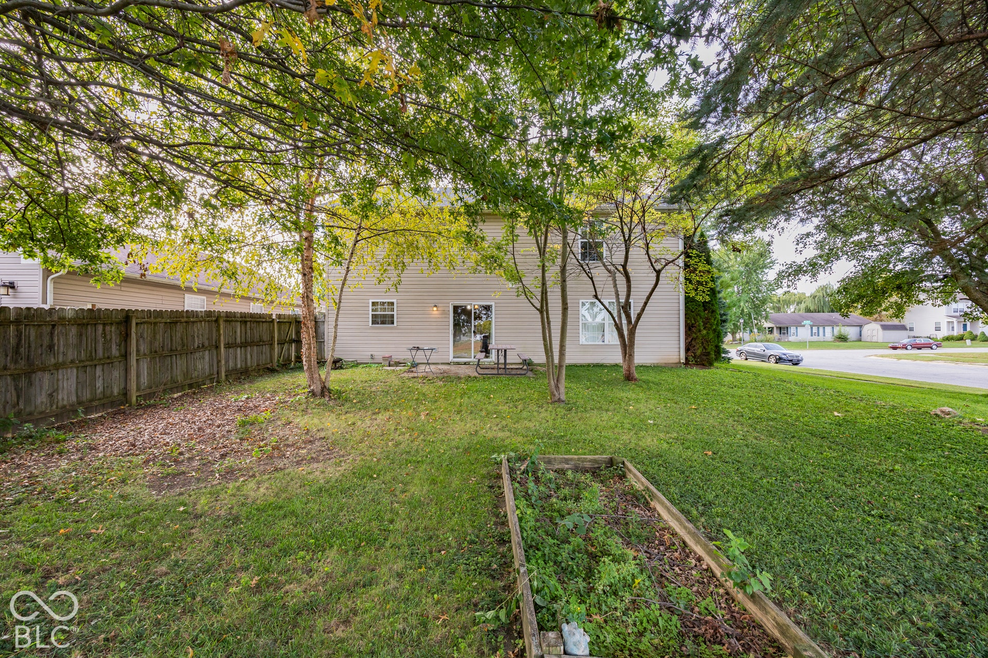 Expansive backyard featuring a privacy fence, established trees, and a raised garden bed