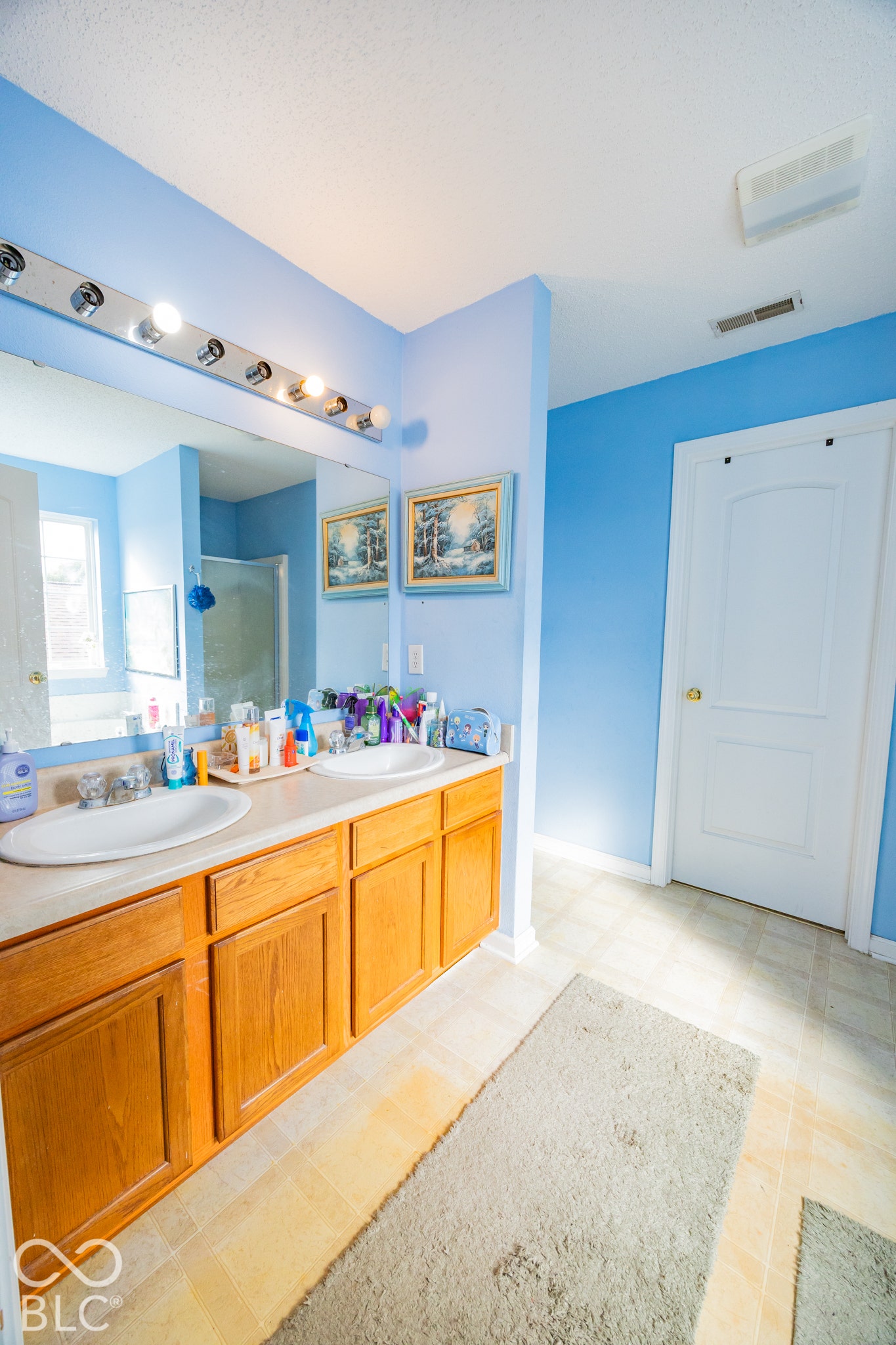 Bright, spa-inspired primary bathroom featuring vibrant blue walls, wood-finish vanity cabinetry with ample storage, white ceramic vessel sink, illuminated mirror with integrated lighting, and tile shower enclosure with glass surround