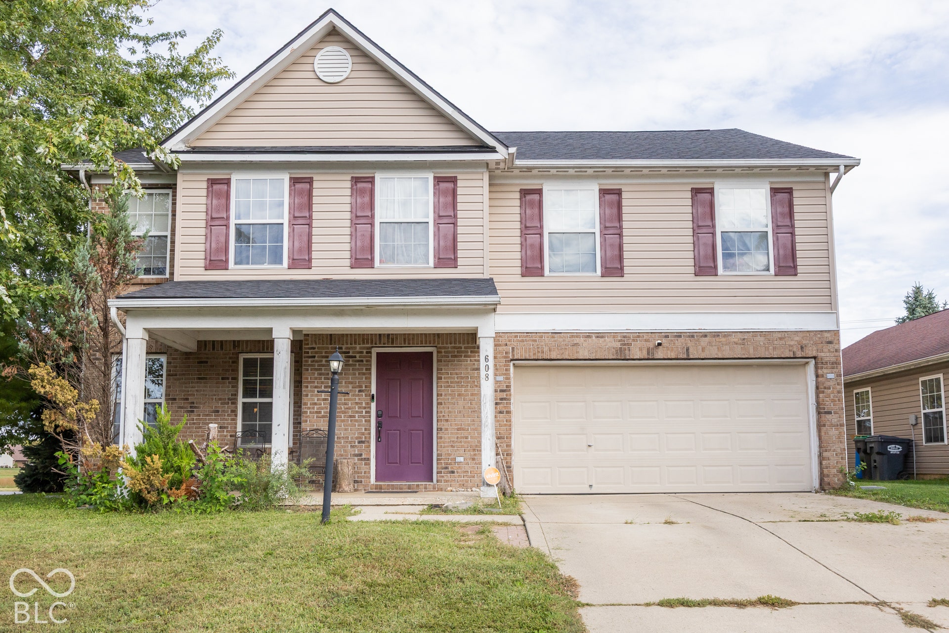 Two-story residence featuring a covered entry, attached two-car garage, brick and siding exterior, and a prominent front door