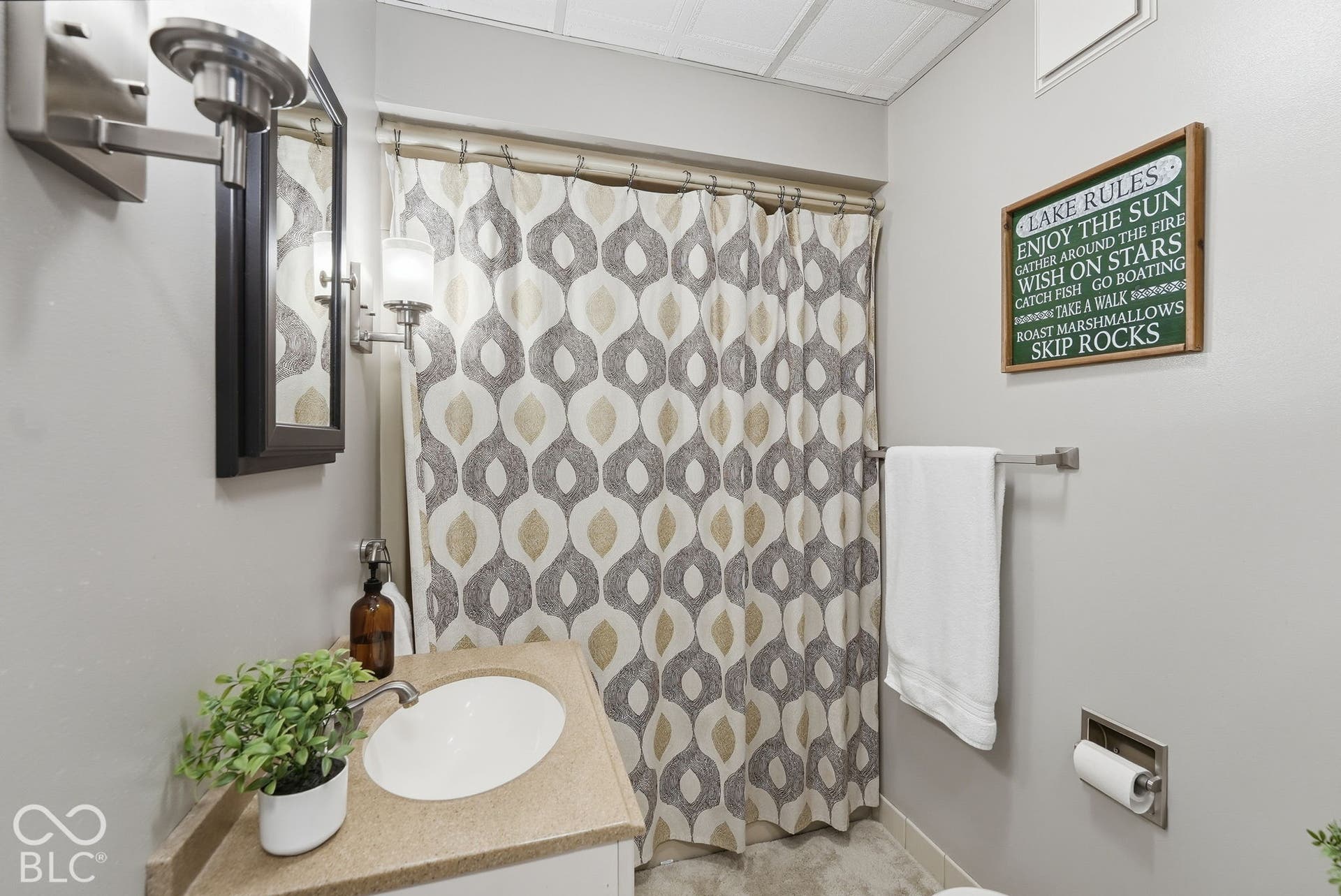 Bathroom featuring a vanity with an integrated sink and light-toned countertop, wall-mounted sconce lighting, and a mirror with a dark frame