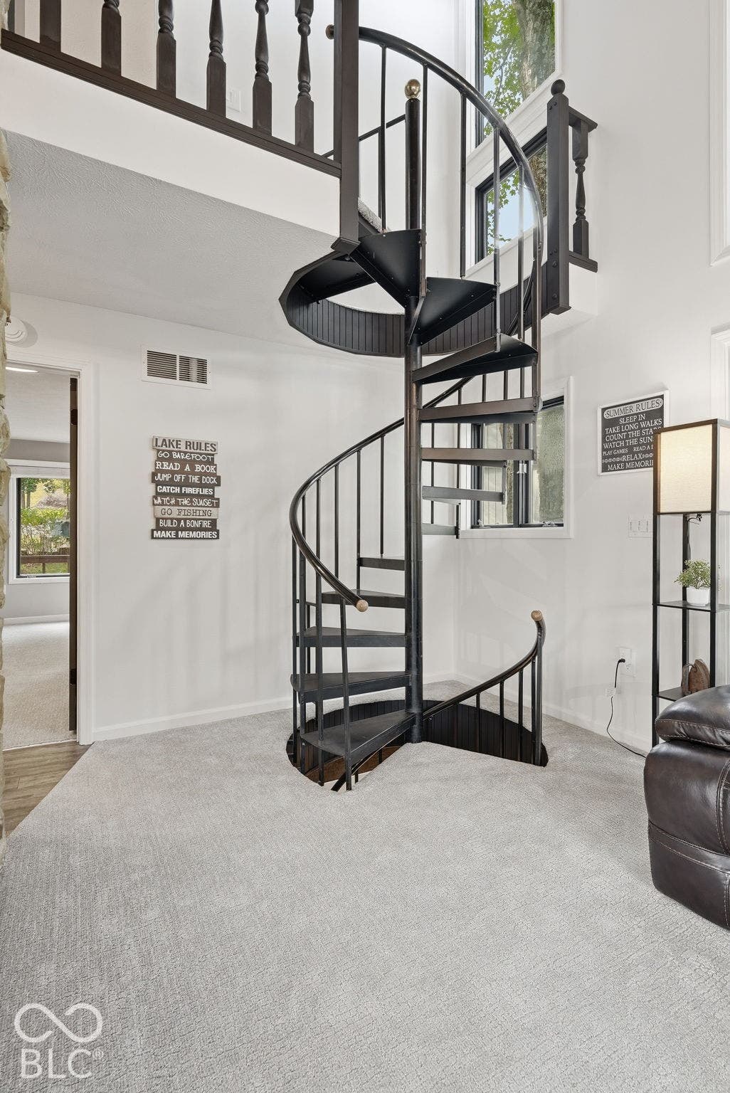 Black metal spiral staircase with wood-finish handrail, light gray carpet, and white walls