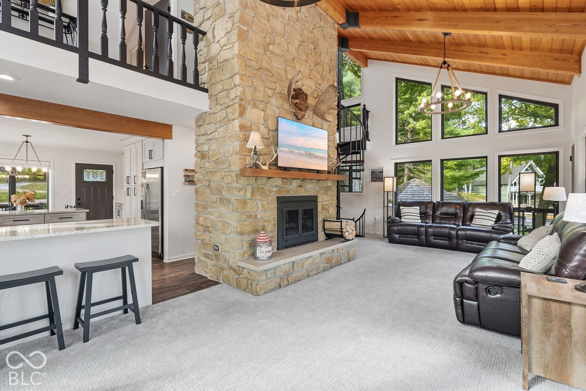 Vaulted wood-paneled ceilings, a stone fireplace, and a spiral staircase, with extensive window walls, and a kitchen island with stone countertops