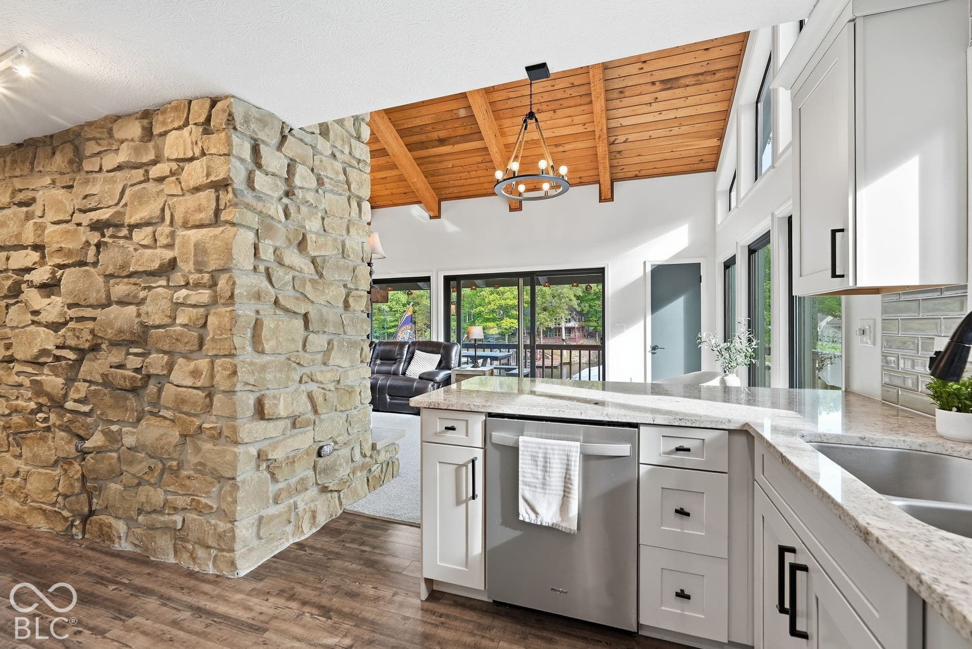 Wood-finish flooring, stone accent wall, vaulted wood-plank ceiling, white cabinetry with dark hardware, and a stainless steel dishwasher