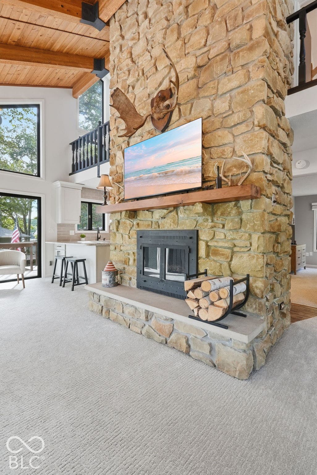 Stone fireplace with hearth, wood mantle, exposed wood beams, and a vaulted ceiling