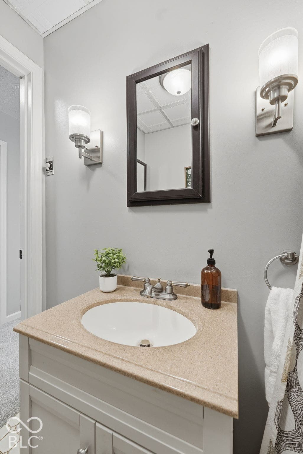 Light-colored vanity with built-in sink, dual wall sconces, framed mirror, and chrome fixtures