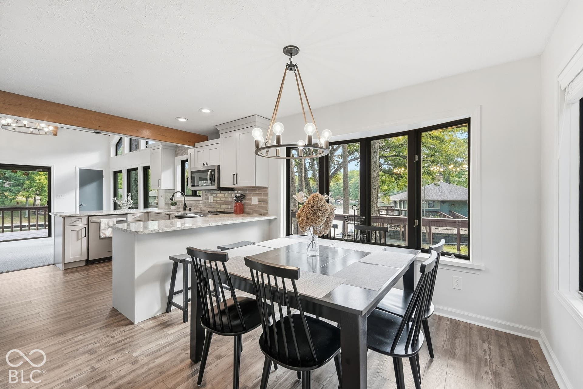 Open-concept kitchen and dining area featuring wood-finish flooring, white cabinetry, a kitchen island with seating, a large bay window, and a contemporary chandelier