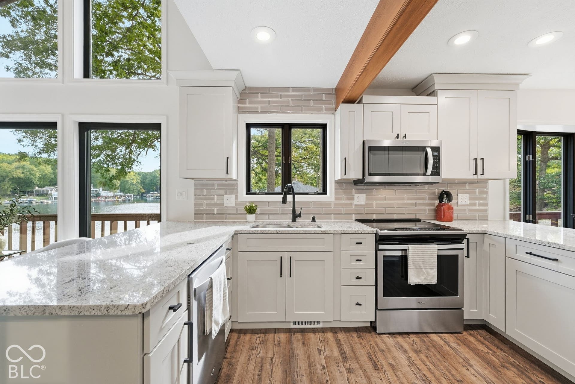Kitchen featuring white cabinetry, light-toned countertops, wood-finish flooring, stainless steel appliances, and a tiled backsplash