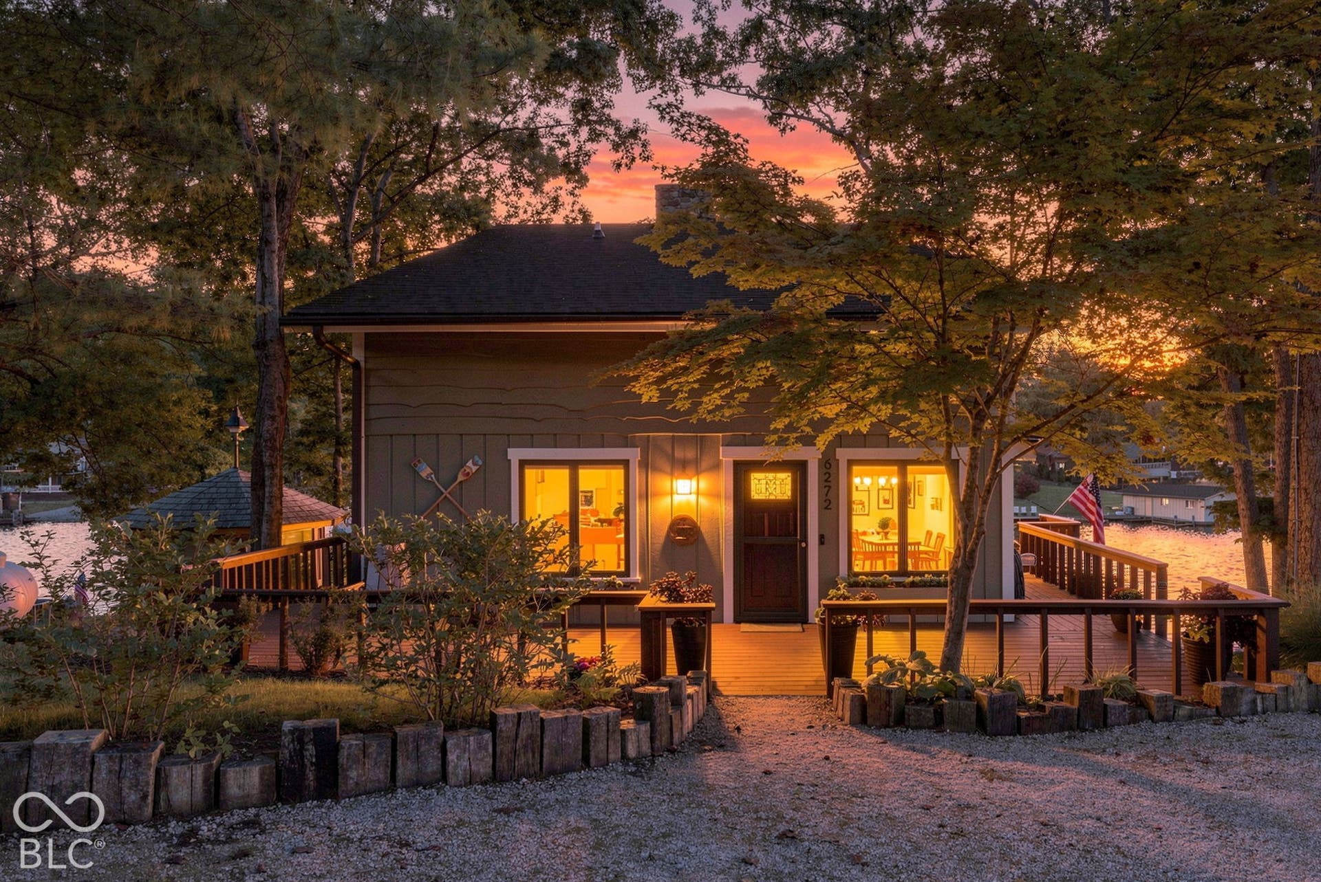Expansive deck with wood railing, gravel driveway, mature trees, and landscaping
