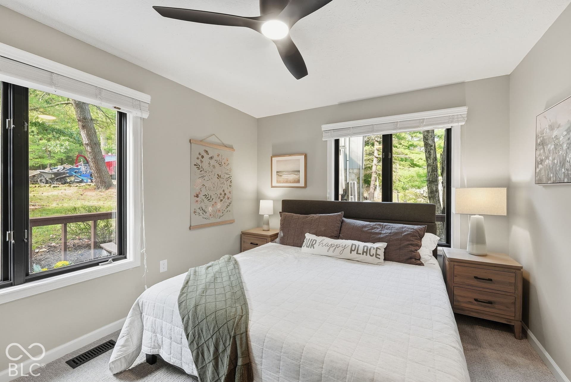 Neutral painted walls with built-in ceiling fan, two large windows with black trim, and light grey carpeting