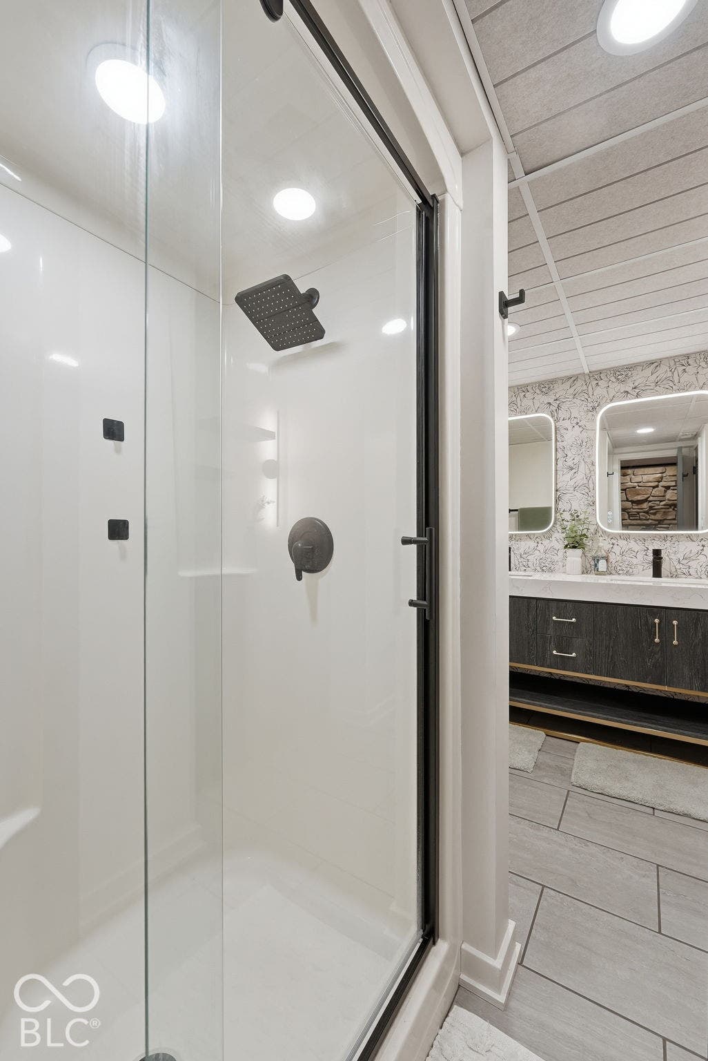Enclosed shower with a dark bronze rainfall shower head, integrated body sprays, and a sliding glass door
