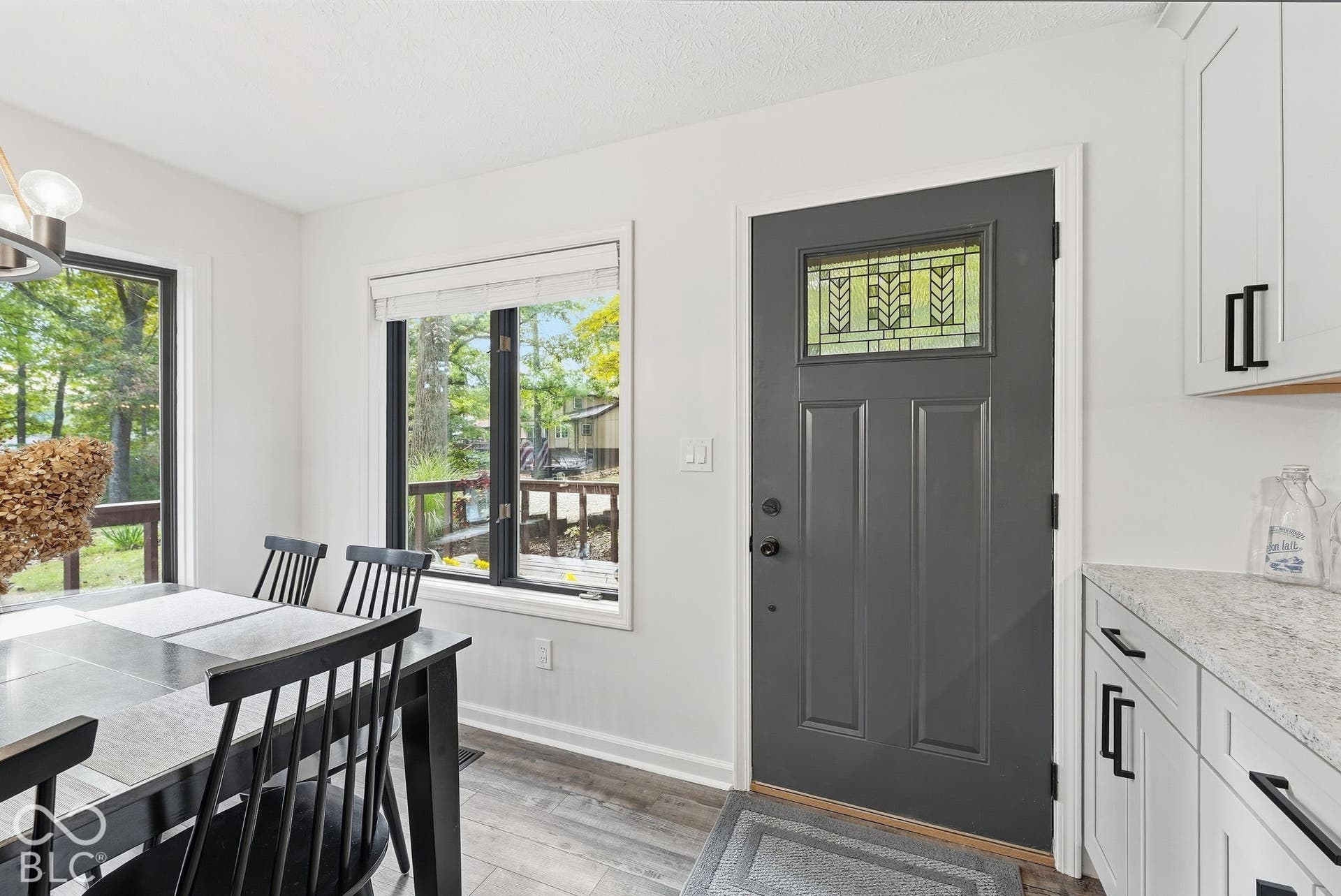 Gray paneled entry door with decorative glass insert, white cabinetry with black hardware, white countertops, and wood-finish flooring