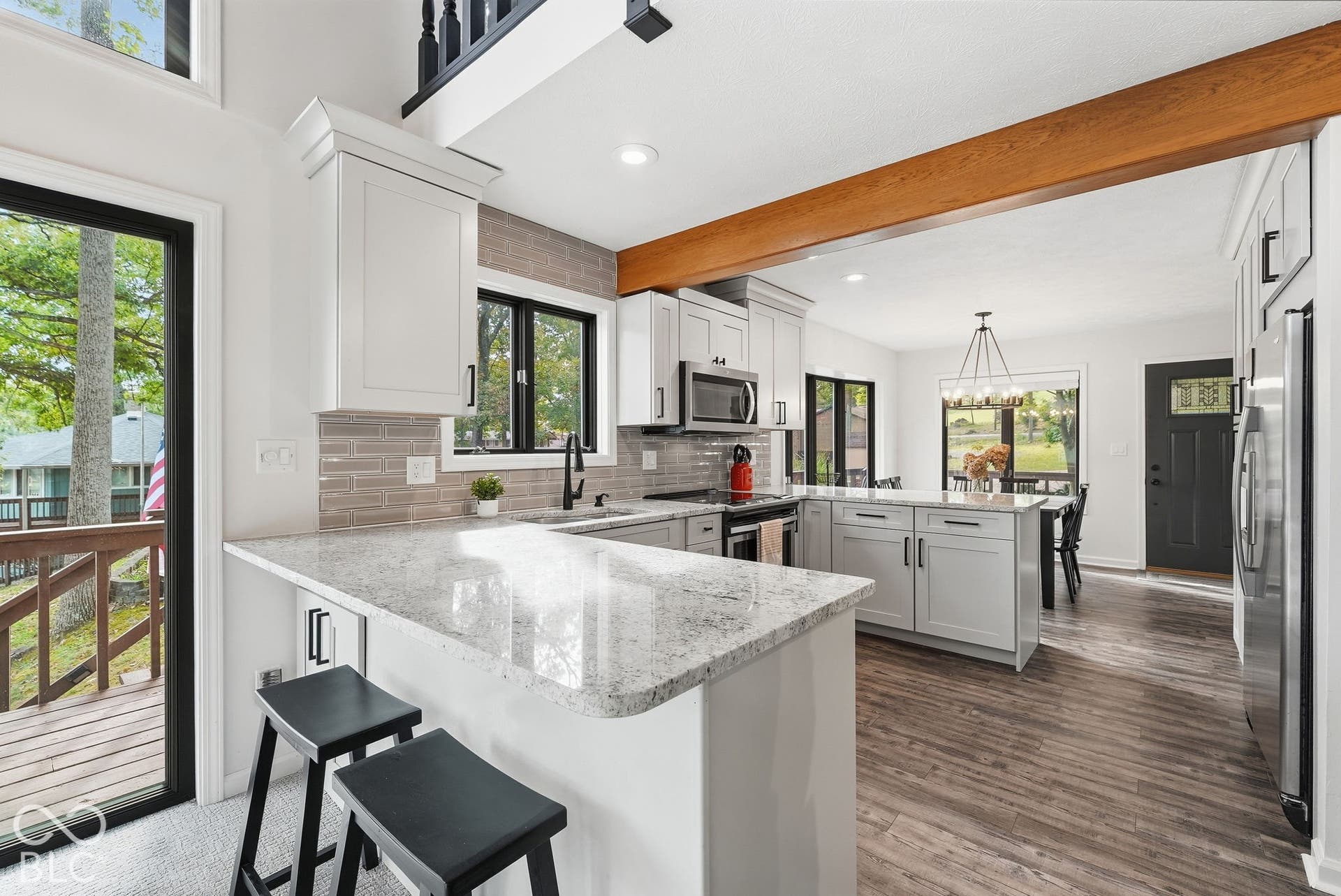 Kitchen featuring light-toned cabinetry, stainless steel appliances, wood-finish flooring, a wood beam accent, and a light-toned countertop with a breakfast bar