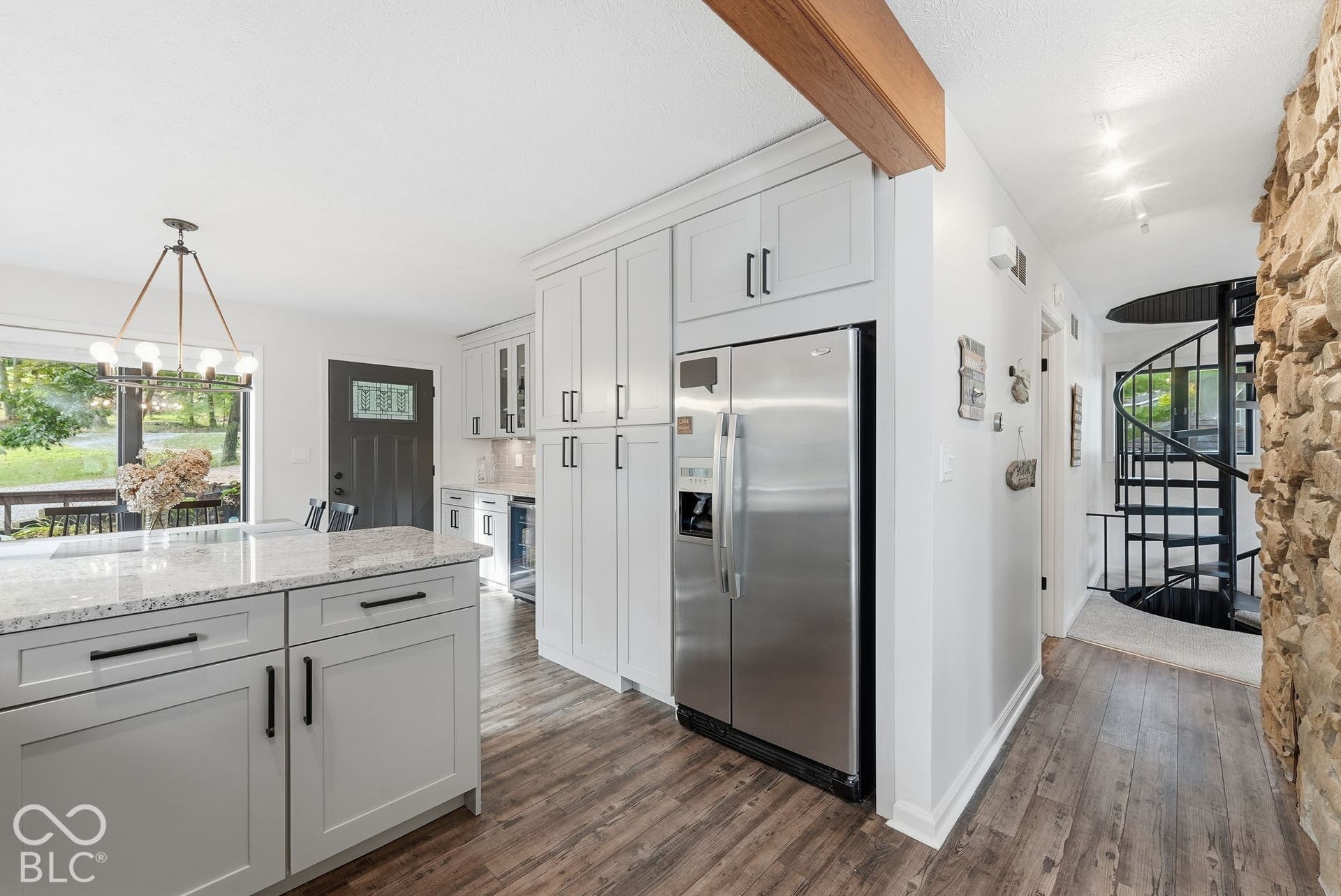 Kitchen featuring an island with stone-finish countertop, stainless steel refrigerator, white cabinetry, and wood-finish flooring