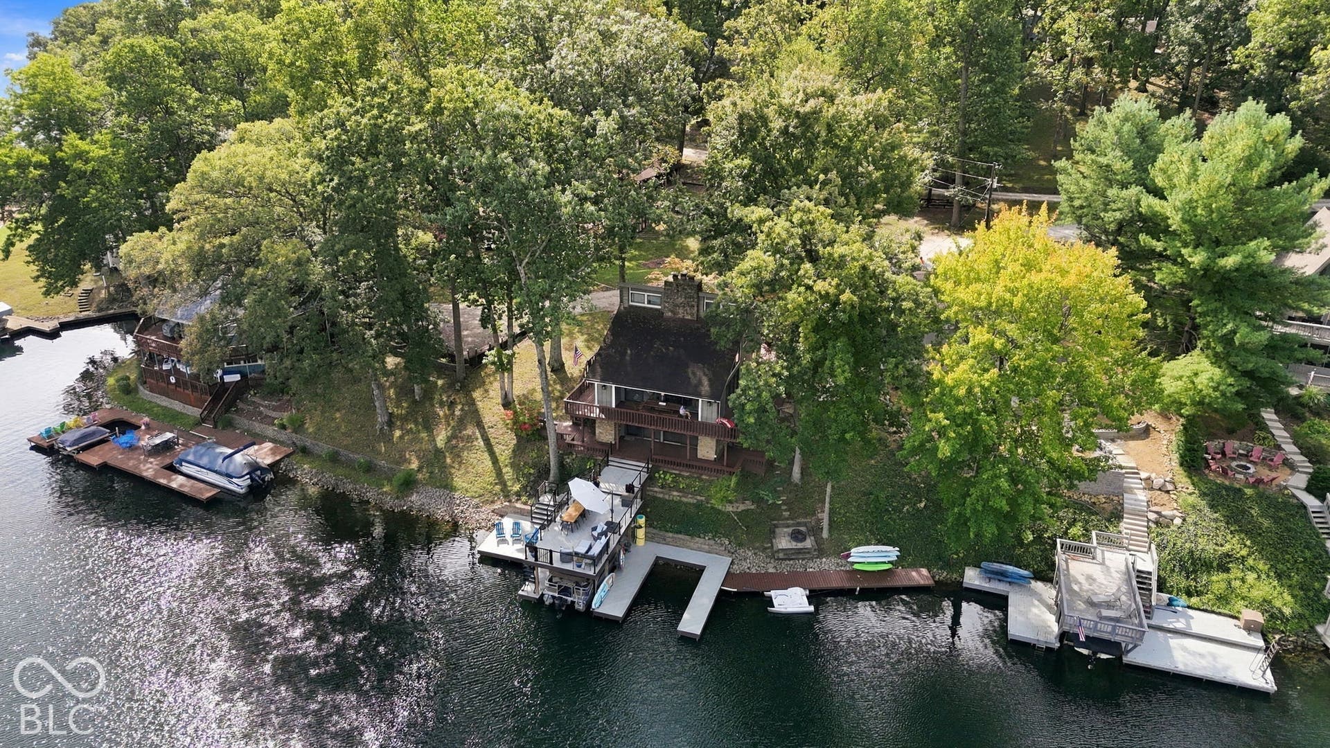 Waterfront property featuring extensive mature trees, a multi-level dwelling with an exterior balcony, multiple private boat docks, and a paved stairway leading to the water