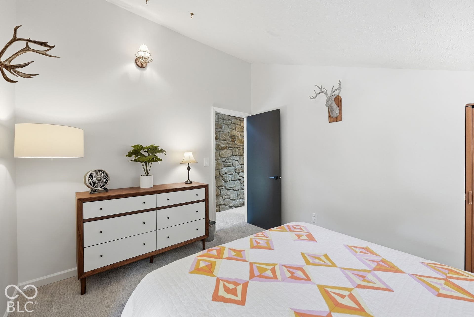 Vaulted ceiling with sconce lighting, stone accent wall, and built-in wood-finish cabinetry