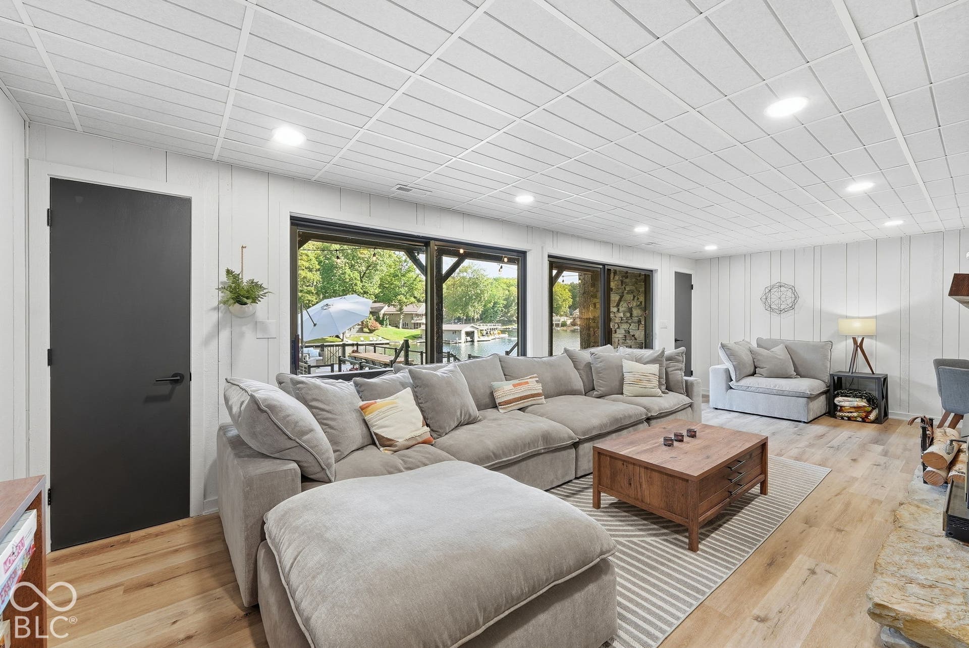 Expansive living area with wood-finish flooring, white shiplap walls, and a grid-patterned ceiling with recessed lighting