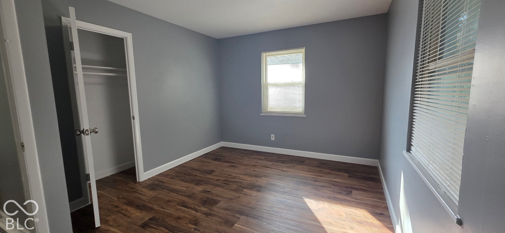 Wood-finish flooring with crisp white trim, a built-in closet, and a window with blinds