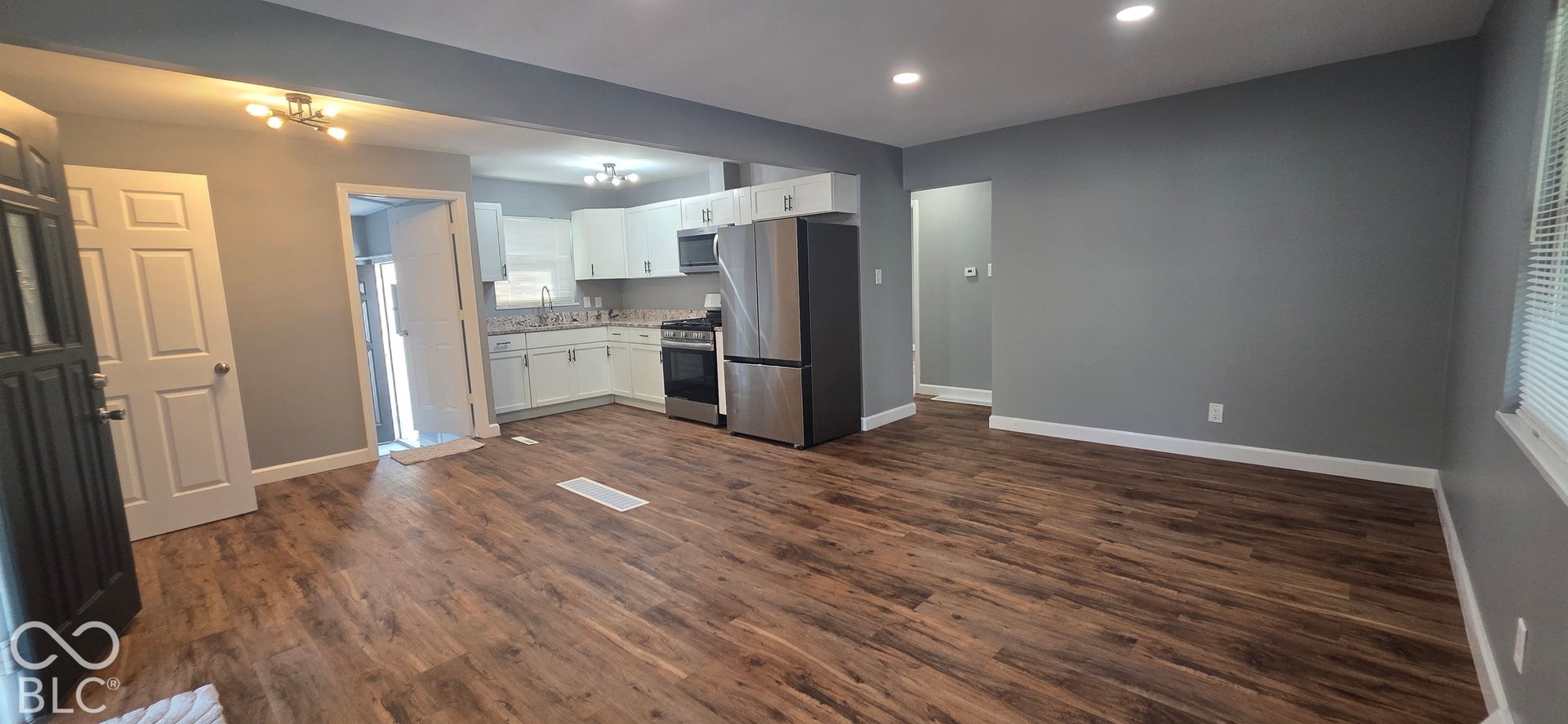 Expansive wood-finish flooring throughout, recessed lighting, white cabinetry, stainless steel appliances, and a tiled backsplash