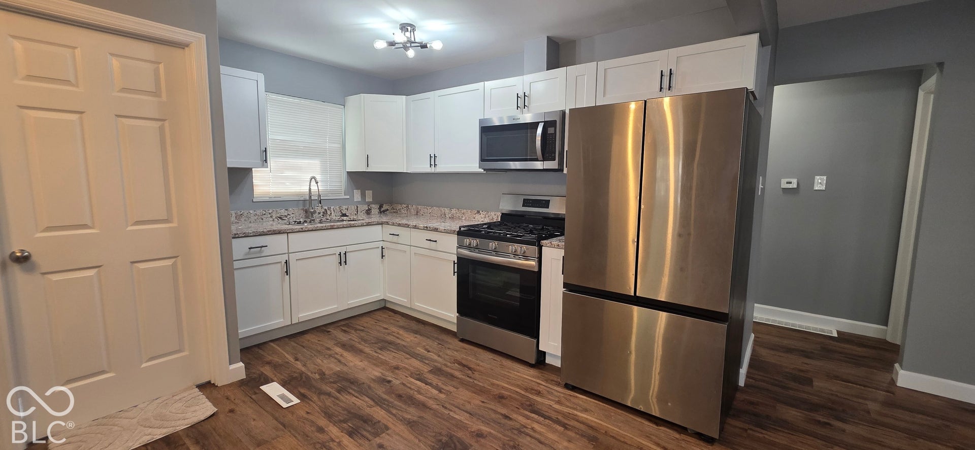 Updated kitchen featuring wood-finish flooring, white cabinetry, stainless steel appliances, and a built-in microwave