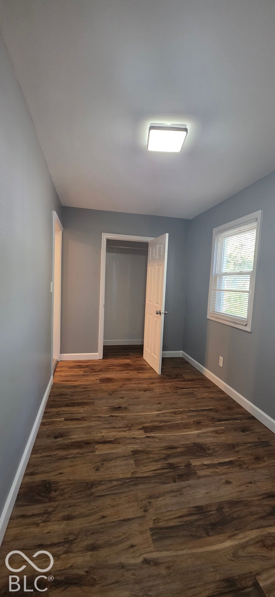 Wood-finish flooring, neutral gray walls, white trim, and a window with white casing