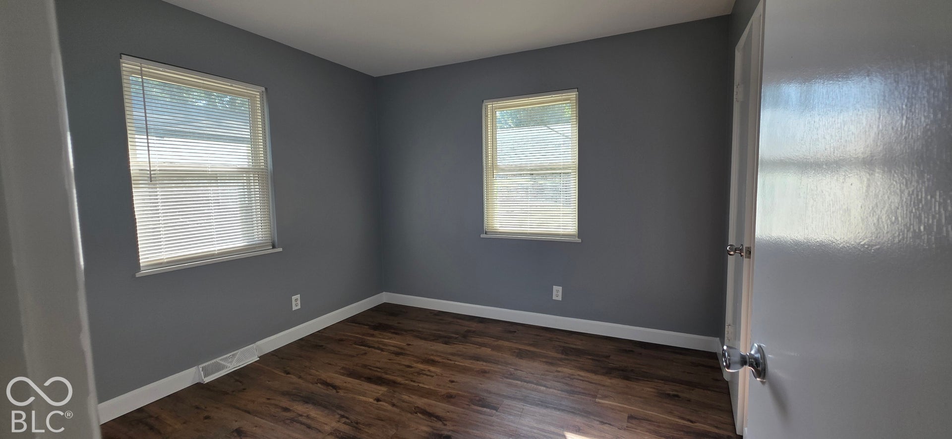 Wood-finish flooring, two windows with blinds, and neutral grey wall paint