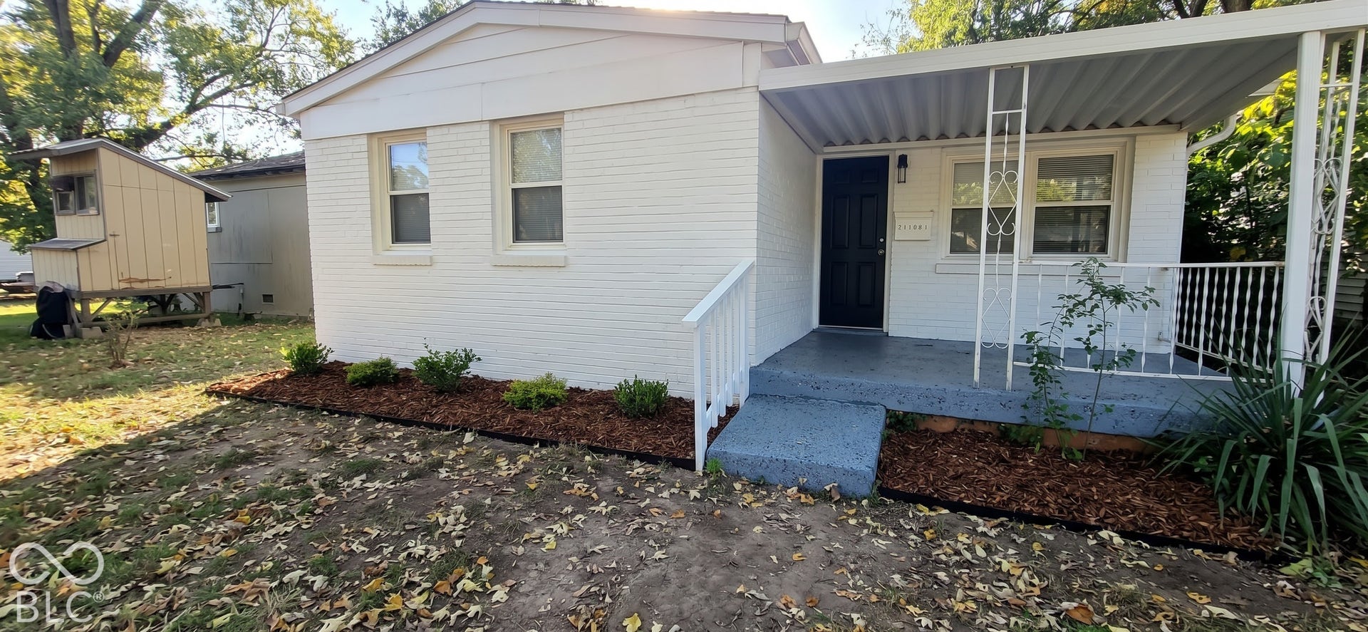 White painted brick exterior with a covered front porch, dark gray painted concrete steps, white porch railing, and landscaped front beds