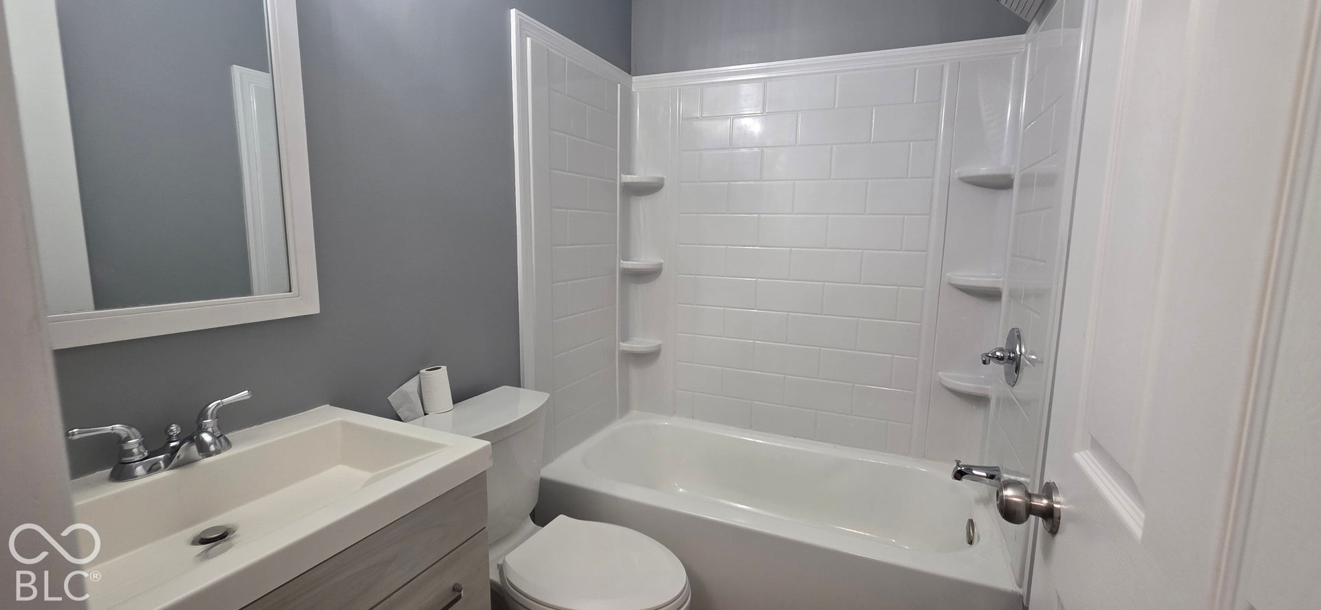 Bathtub with integrated shelving, chrome fixtures, and subway tile-style surround