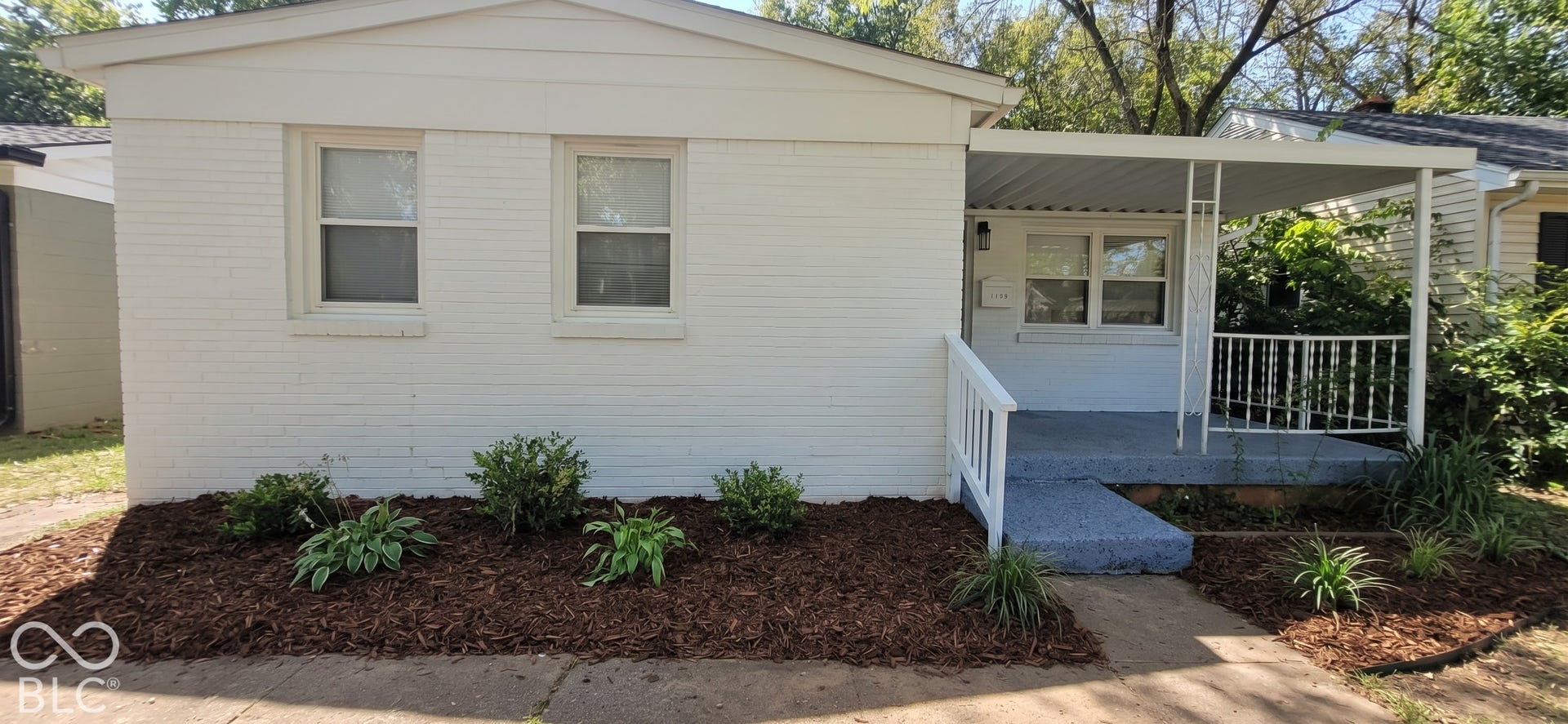 White painted brick exterior with a covered porch, white railing, and decorative porch columns