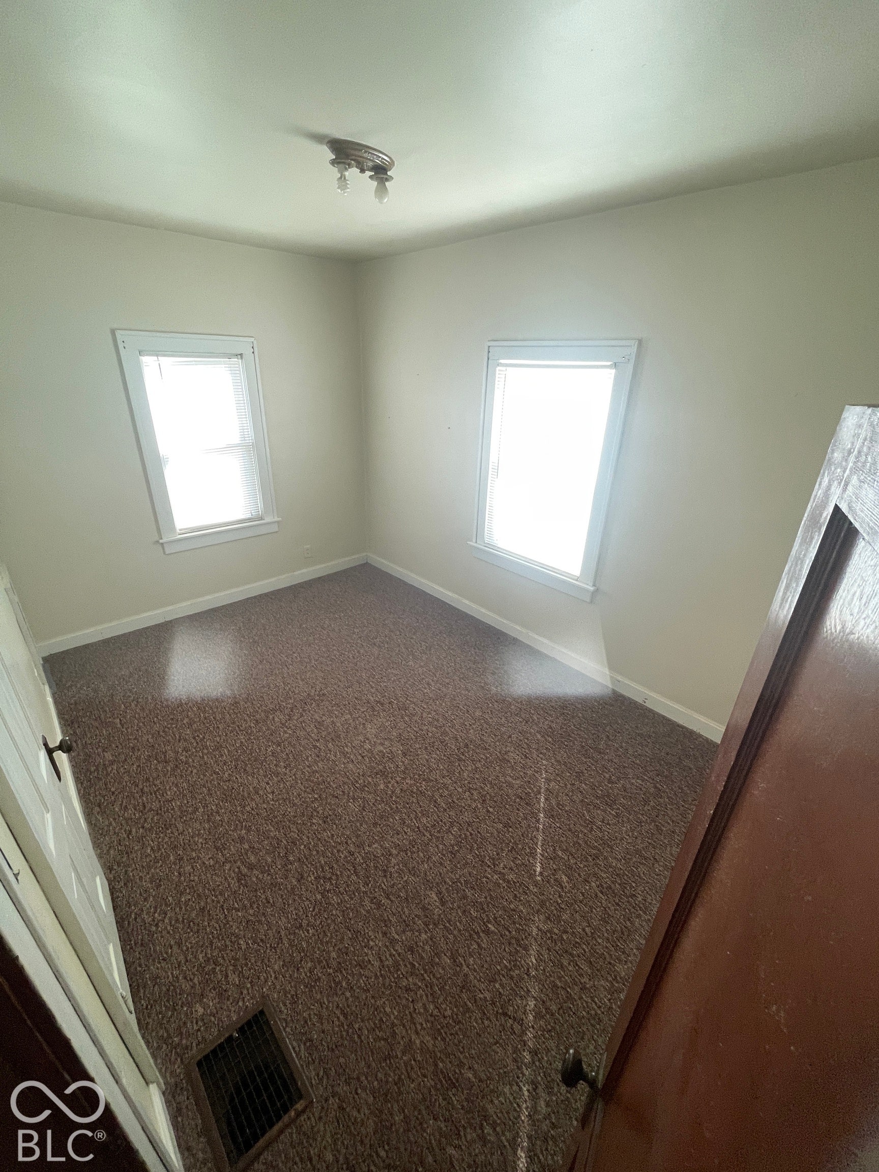 Carpeted flooring, two windows with white trim, and a ceiling-mounted light fixture