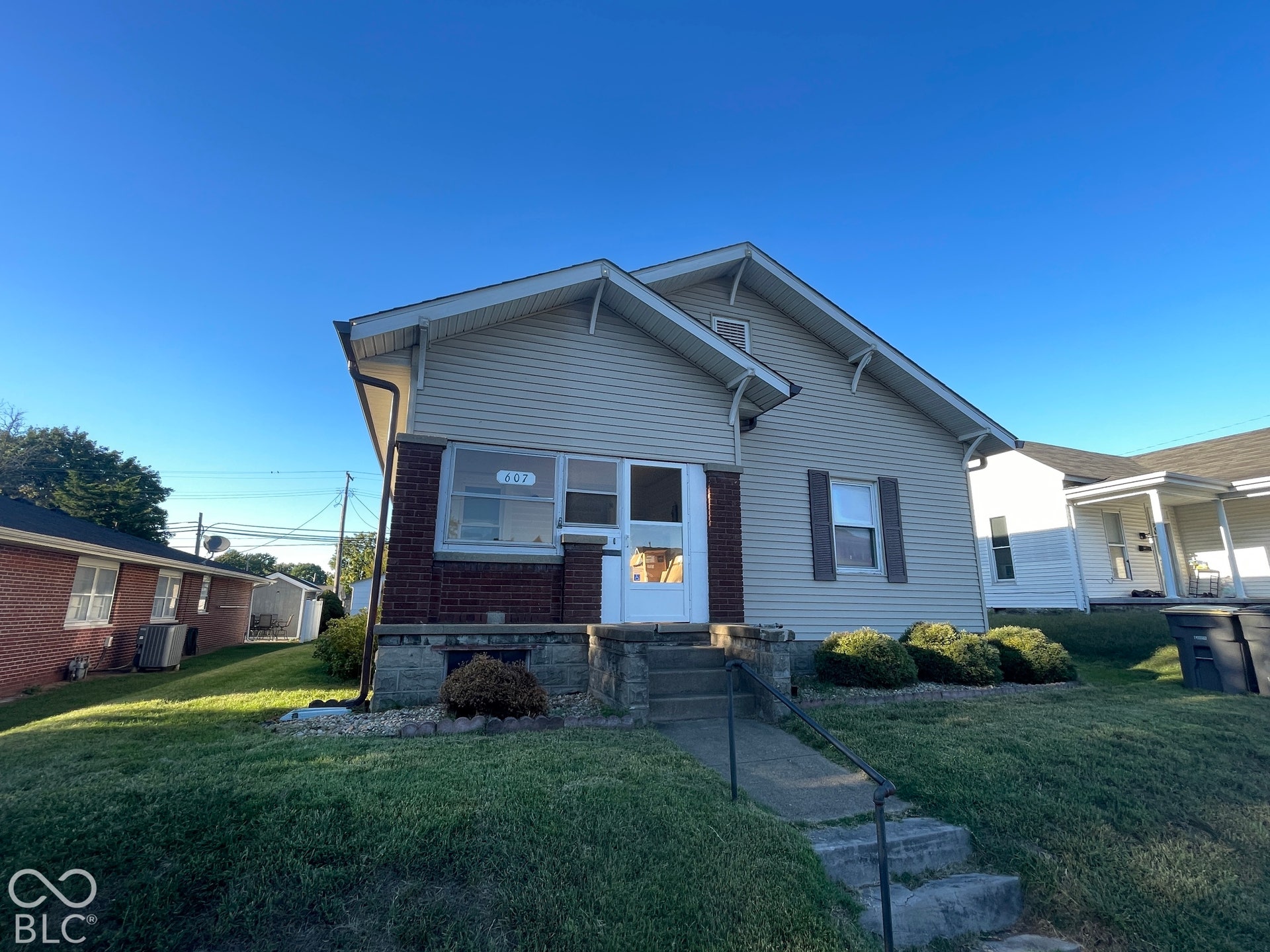 Siding exterior with brick detailing, concrete front steps with metal railing, and established front landscaping
