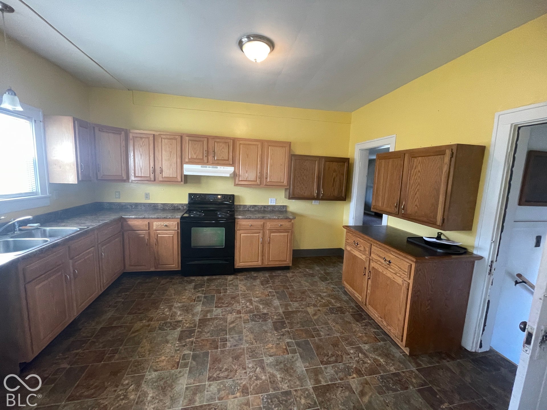 Kitchen featuring ample wood-finish cabinetry, dark countertops, a black range with an overhead vent, and durable tile-patterned flooring