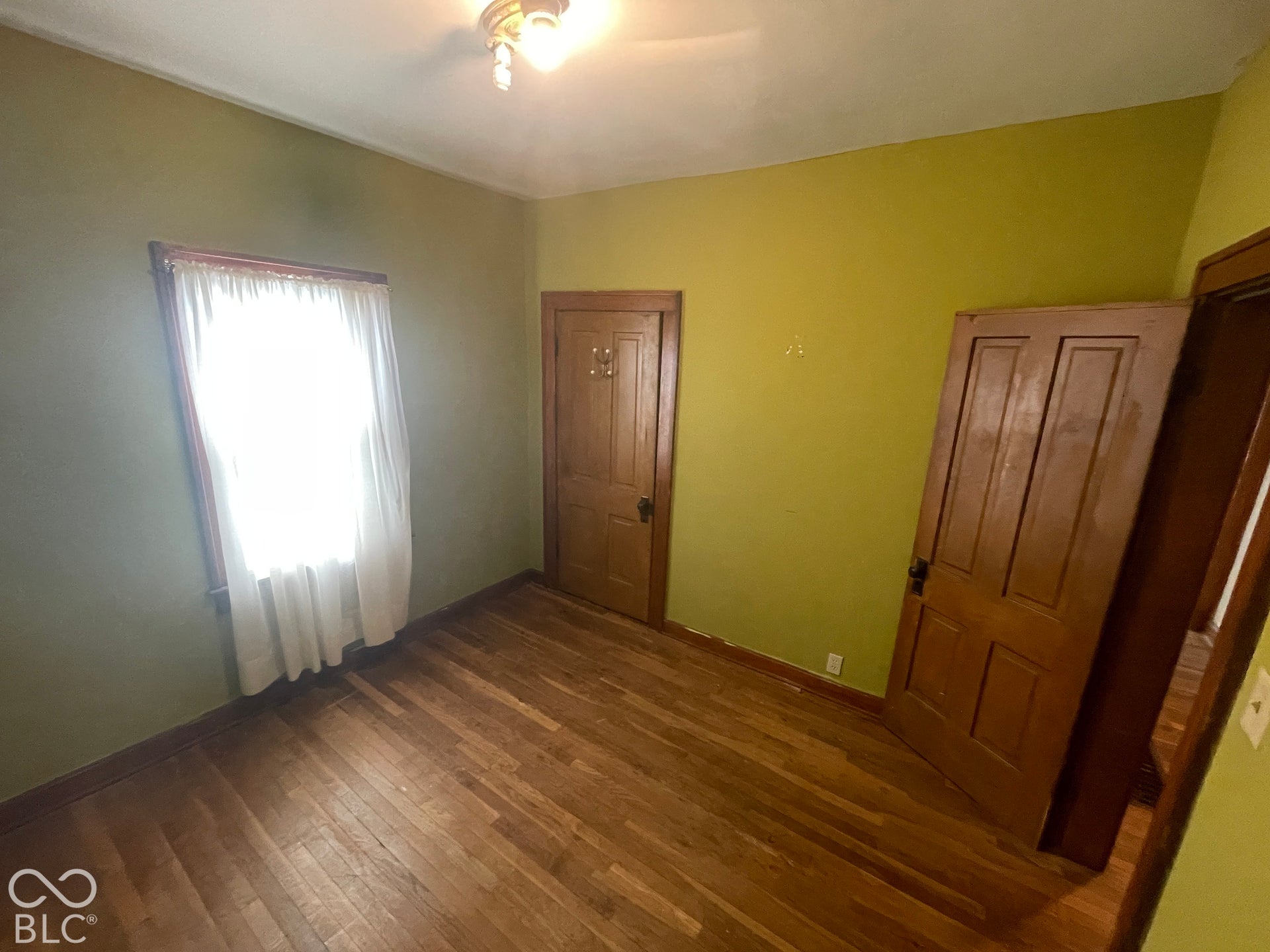 Wood-finish flooring with perimeter trim, wood-paneled doors, and a ceiling-mounted light fixture