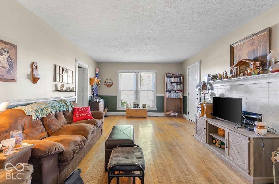 Light wood-finish flooring, white trim, and a white fireplace surround with a mantel