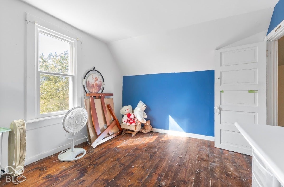 Wood-finish flooring with a white trim, featuring a single-hung window, white paneled door, and a partially painted blue wall
