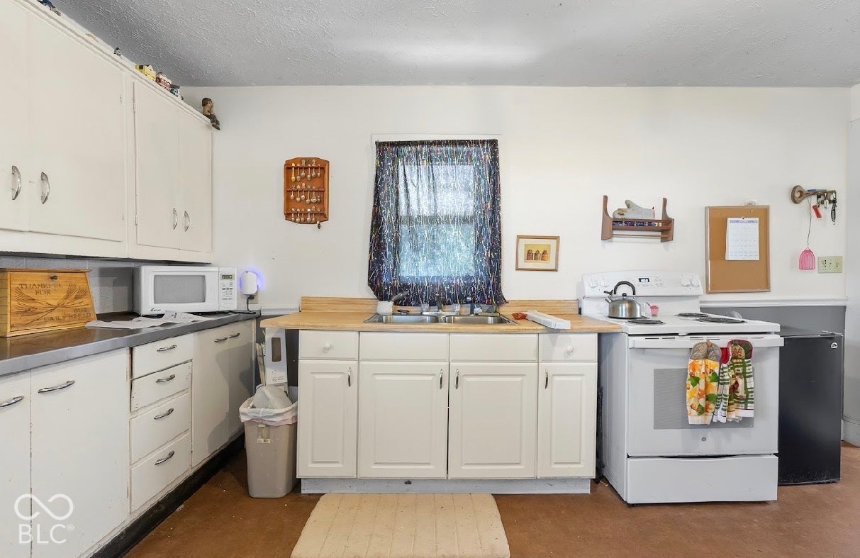 Kitchen featuring white cabinetry, a double basin sink, a window, wood-finish countertops, and an electric range