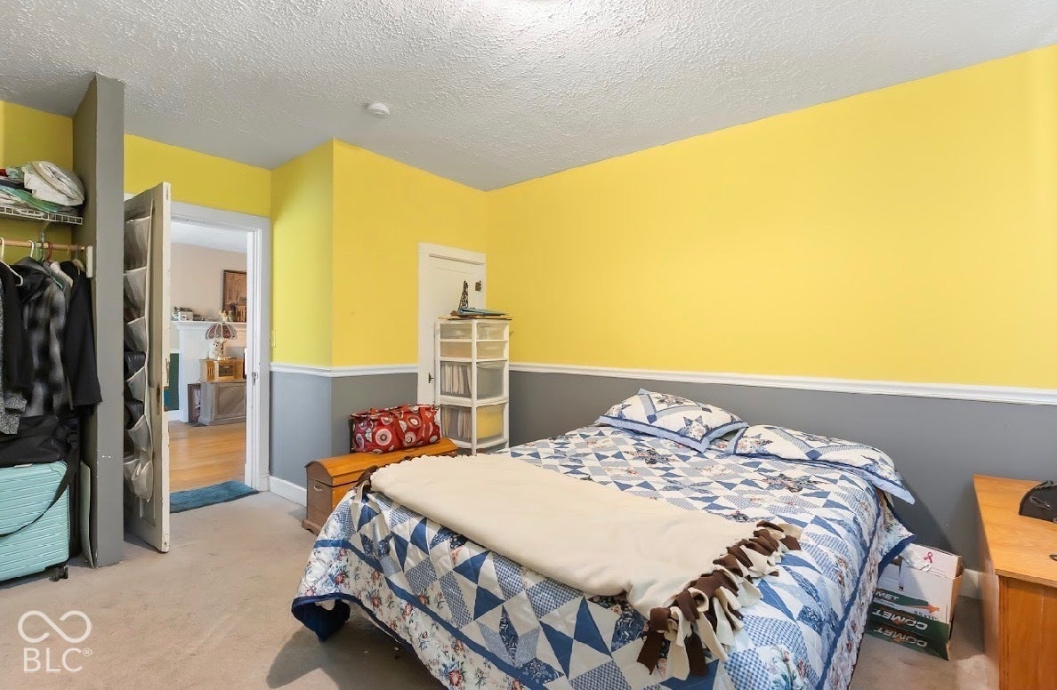 Bright and spacious bedroom featuring sunny yellow walls with gray wainscoting, wood-finish flooring, and ample natural light from multiple windows