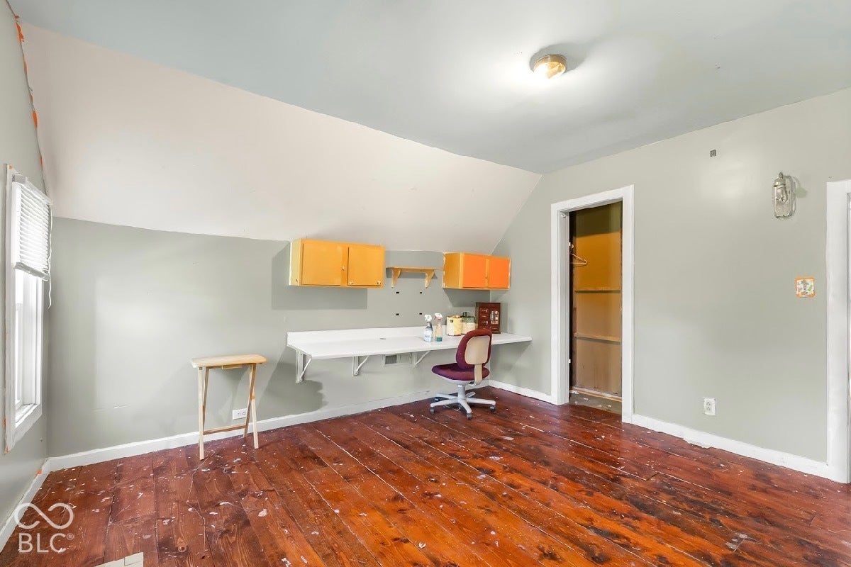 Wood-finish flooring, built-in shelving, mounted cabinetry, window with blinds, and ceiling-mounted light fixture