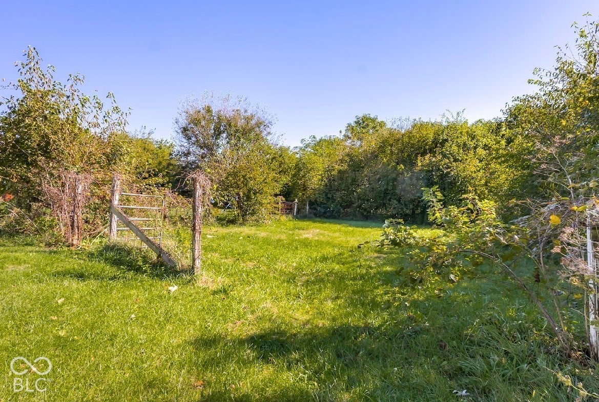Expansive grassy area with a partial wooden fence and varied mature foliage