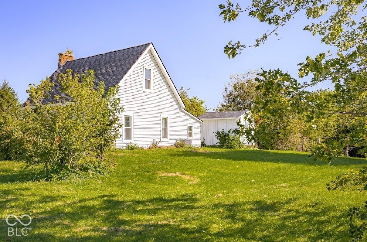 White siding exterior with a dark asphalt shingle roof, brick chimney, and multiple windows