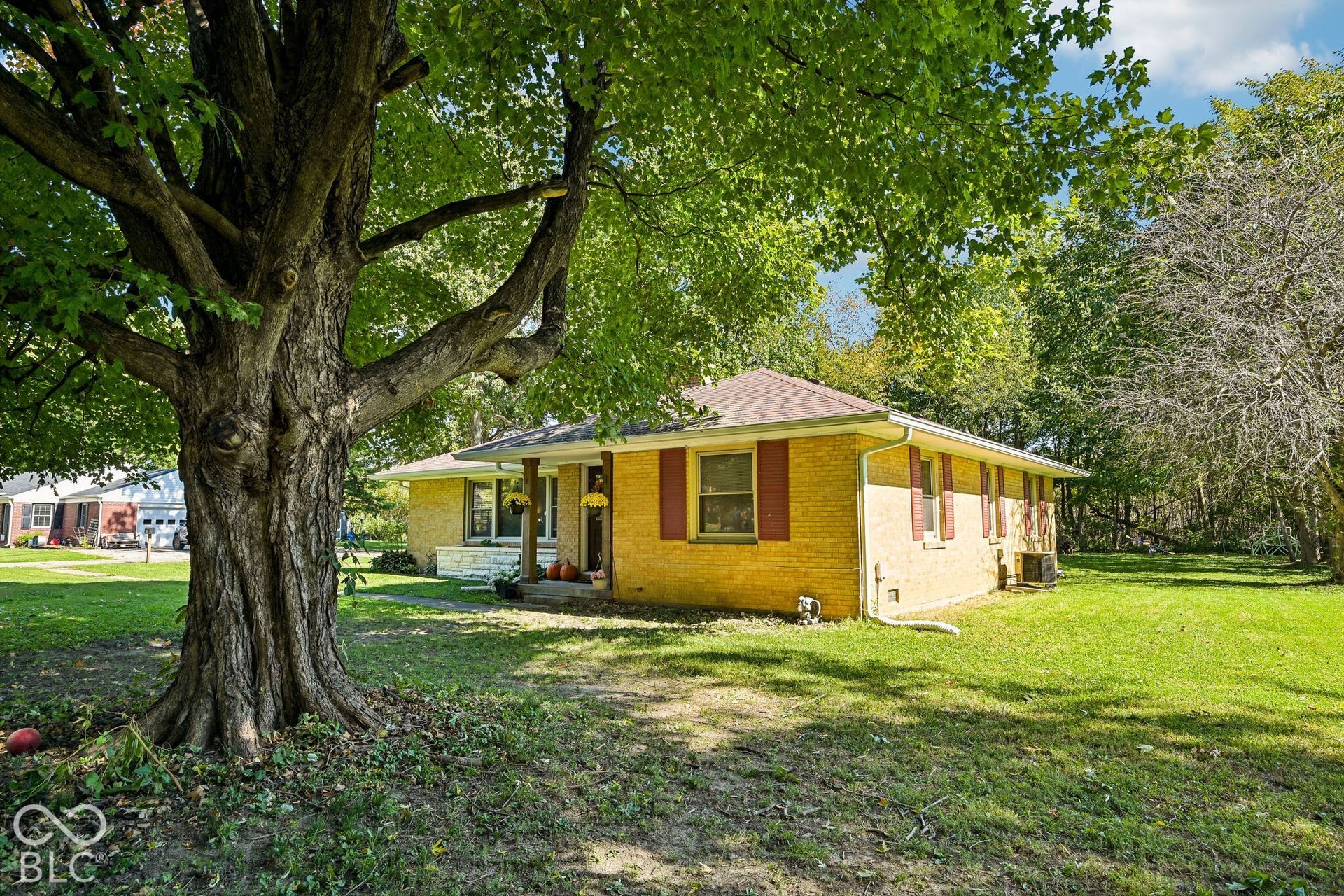 Yellow brick exterior with red shutters, a prominent mature tree, and expansive grassy areas