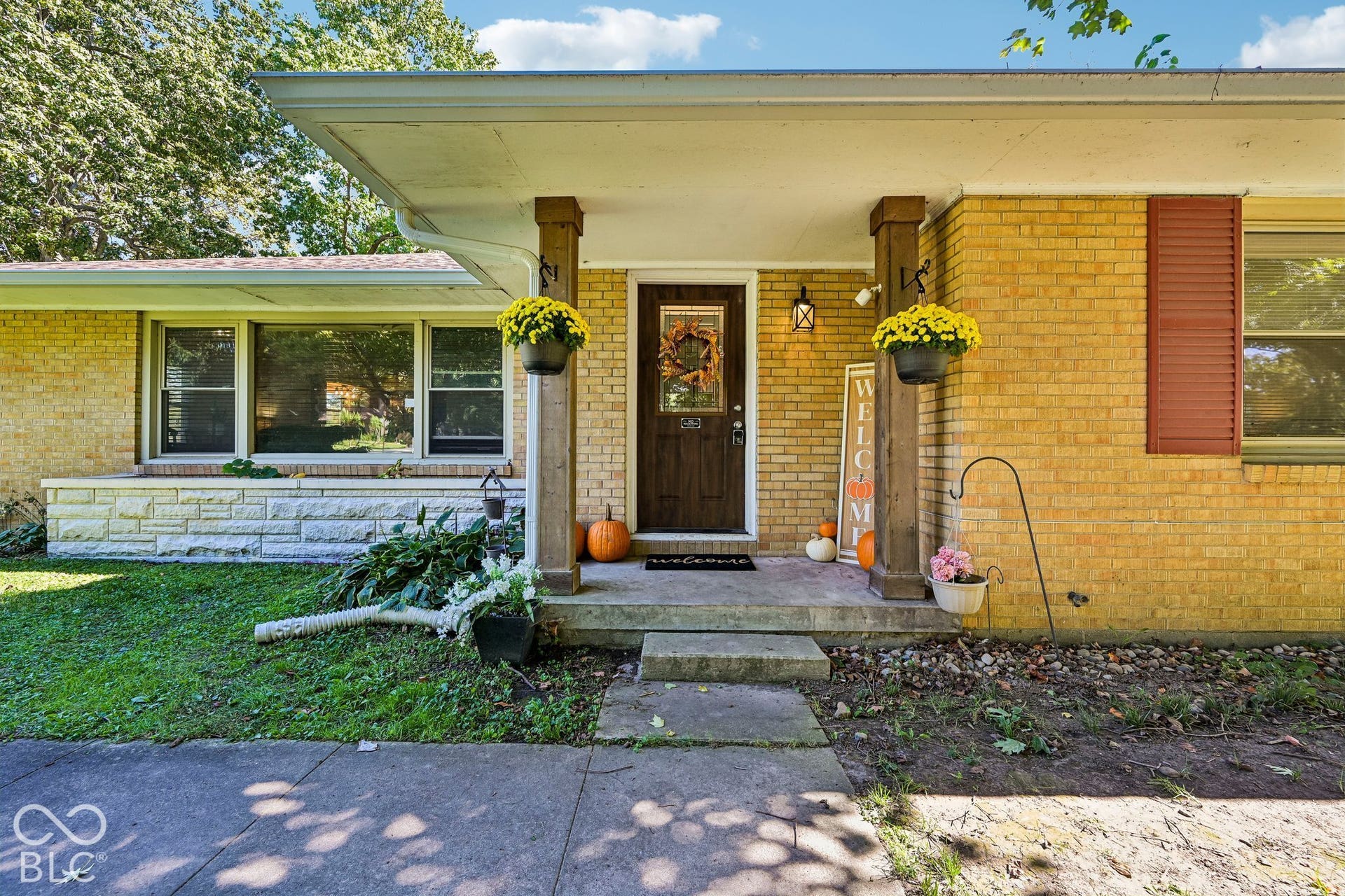Brick exterior with decorative red shutters, covered front porch, and a dark wood-finish entry door with sidelights